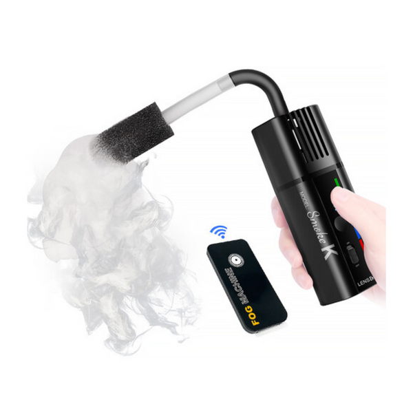 A handheld mini fog machine emitting smoke, with a wireless remote control and a USB-C charging cable.